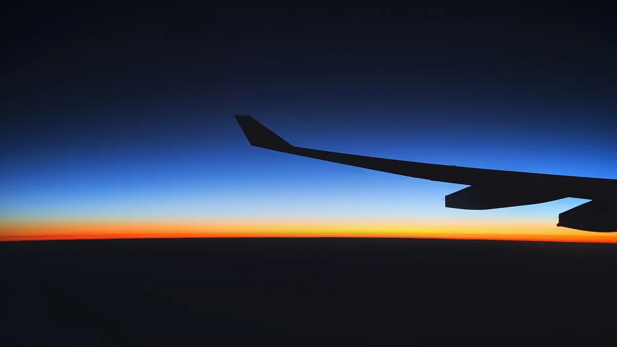 View of an airplane wing against an orange sunset sky